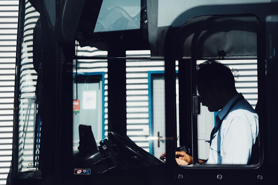 A bus driver seated at the wheel, seen through the open door of the cab.