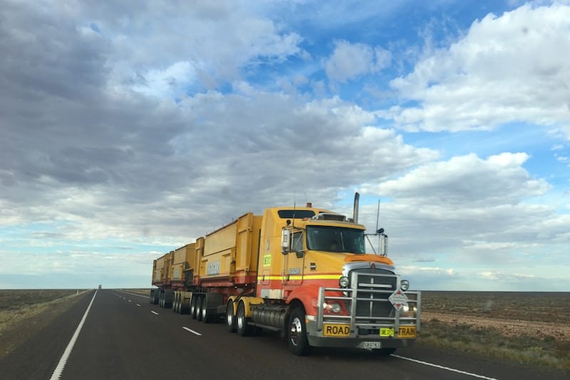An Australian road train travelling along a highway through open country.