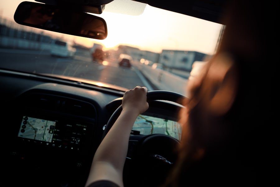 View over a driver's shoulder, hands on the steering wheel, looking down a road at dusk.