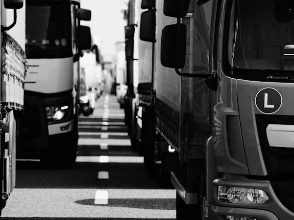 Black and white photograph of heavy trucks queued either side of a dashed road centre line.
