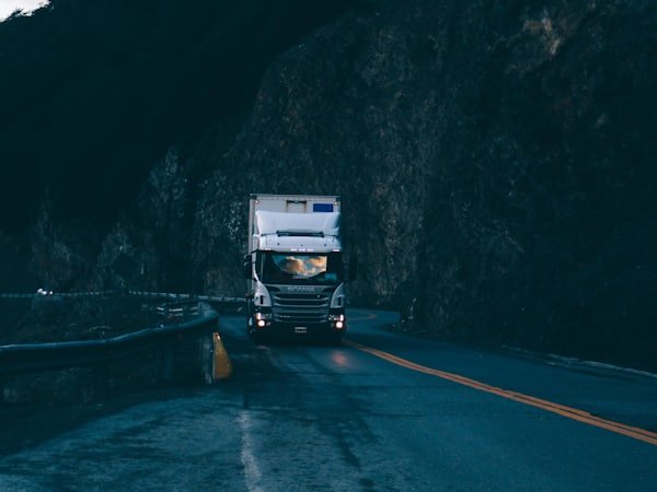 A truck driving on a wet mountain road in low light.