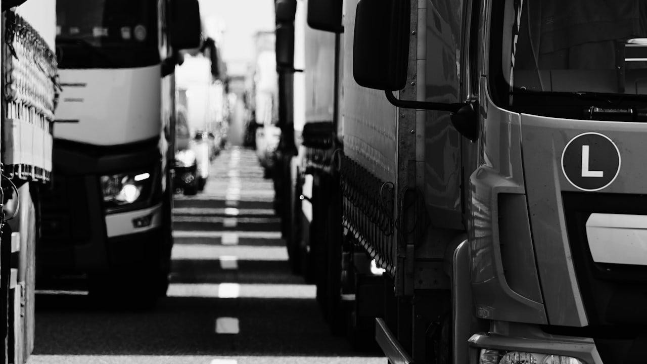 Heavy trucks queued nose to tail on either side of a road's dashed white centre line.
